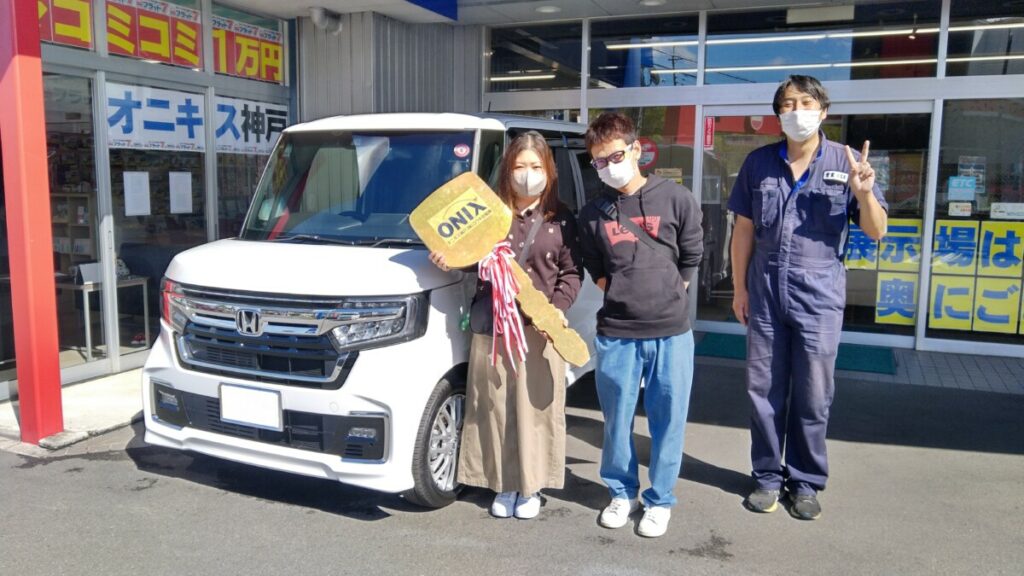 白色の新車N-BOXカスタムターボの御納車写真。N様ご夫妻に担当の小笠原を添えて。